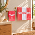 Bombshell Collective Bathroom Duo in Coral featuring the Face Bum Bits bath towel and matching Dry Your Paws hand towel displayed on brass towel rails in a coastal bathroom.