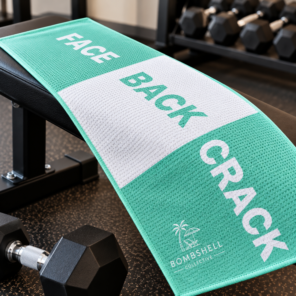 Bombshell Collective Face Back Crack gym towel in aqua displayed on a gym bench, featuring a bold three-section design.