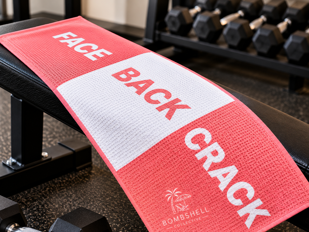 Bombshell Collective Face Back Crack gym towel in coral displayed on a gym bench, featuring a bold three-section design.