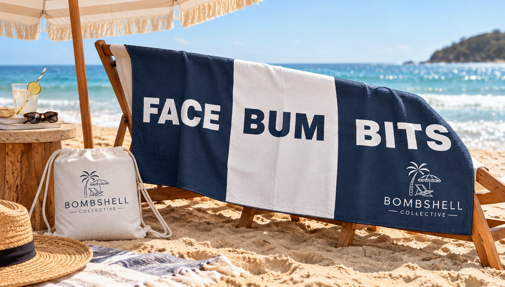 Bombshell Collective Face Bum Bits sand-free waffle microfibre beach towel in deep sea blue laid out on golden sand beside turquoise ocean waves with matching waterproof carry bag.