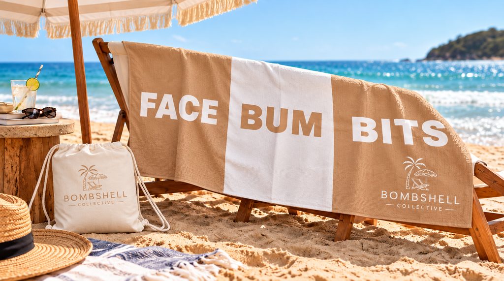 Bombshell Collective Face Bum Bits sand-free waffle microfibre beach towel in sand laid out on golden sand beside turquoise ocean waves with matching waterproof carry bag.