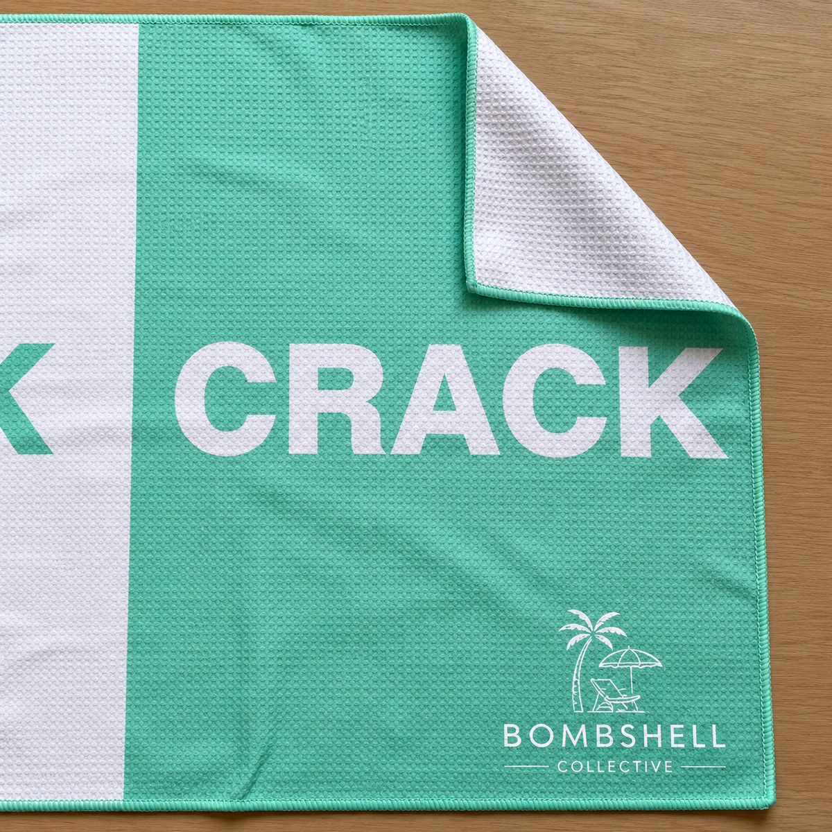 Close-up of Bombshell Collective aqua waffle-textured gym towel showing the folded corner and signature logo.