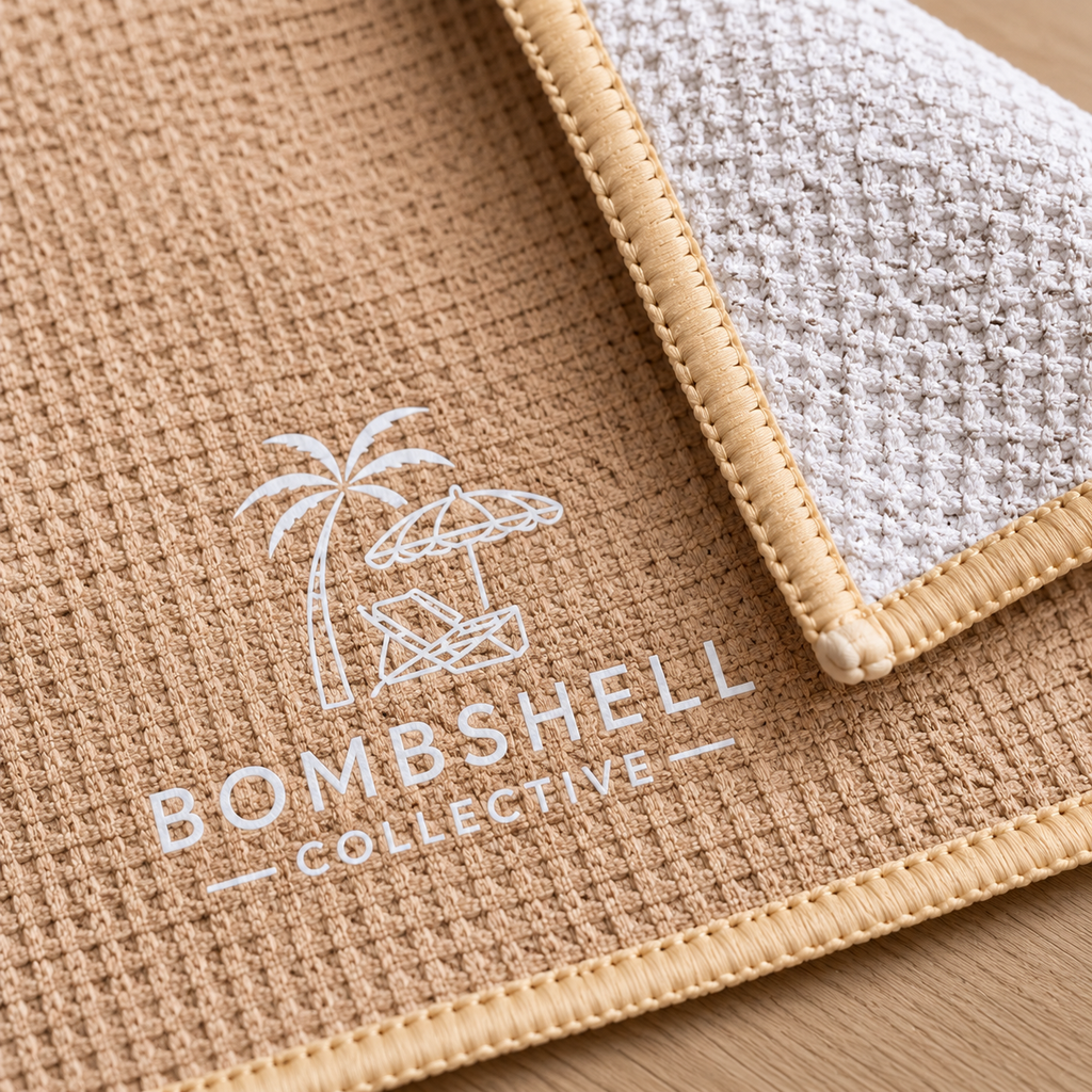 Close-up of Bombshell Collective sand waffle-textured gym towel showing the folded corner, CRACK lettering and signature logo.