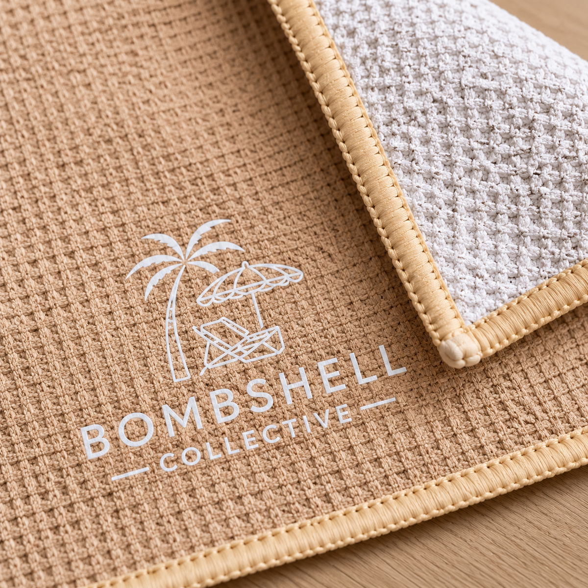 Close-up of Bombshell Collective sand waffle-textured gym towel showing the folded corner, CRACK lettering and signature logo.