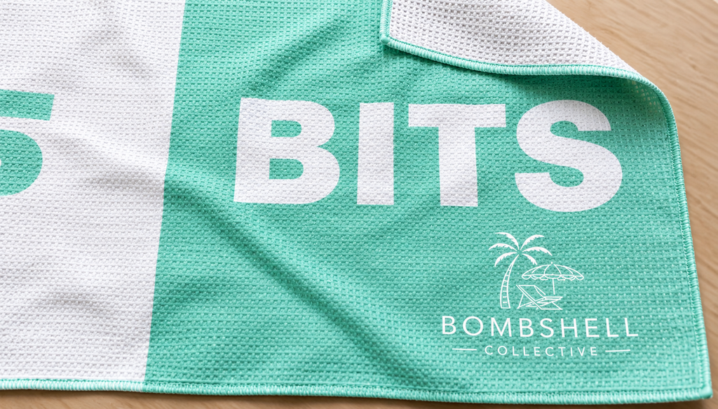 Close-up of the Face Bum Bits beach towel in aqua, showing textured sand-free waffle microfibre fabric, folded corner and Bombshell Collective branding.