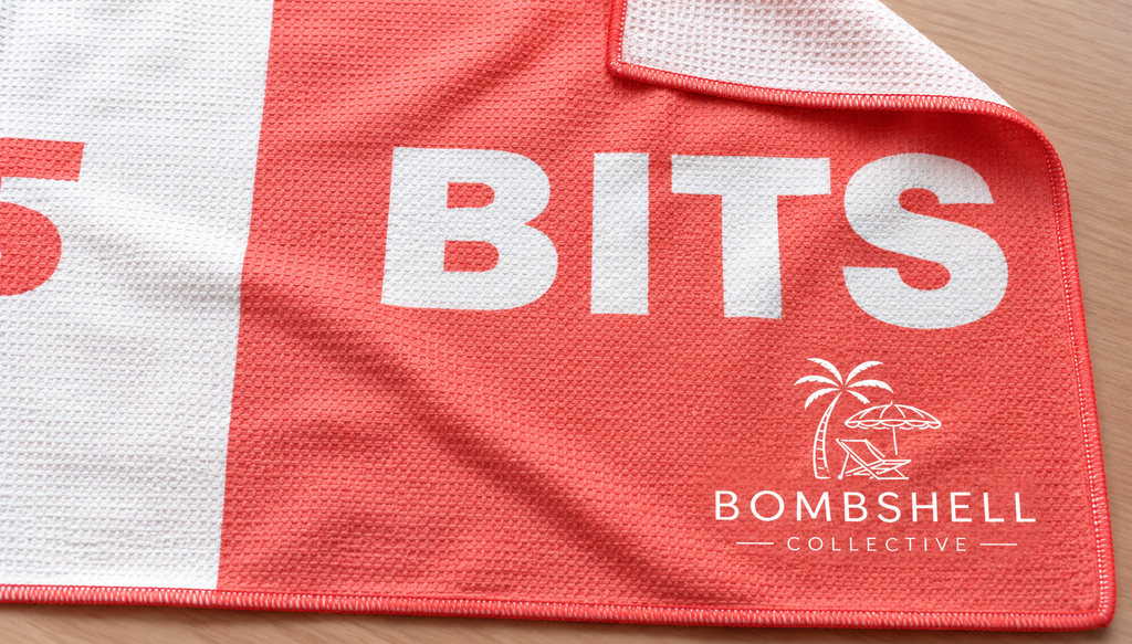 Close-up of the Face Bum Bits beach towel in coral, showing textured sand-free waffle microfibre fabric, folded corner and Bombshell Collective branding.