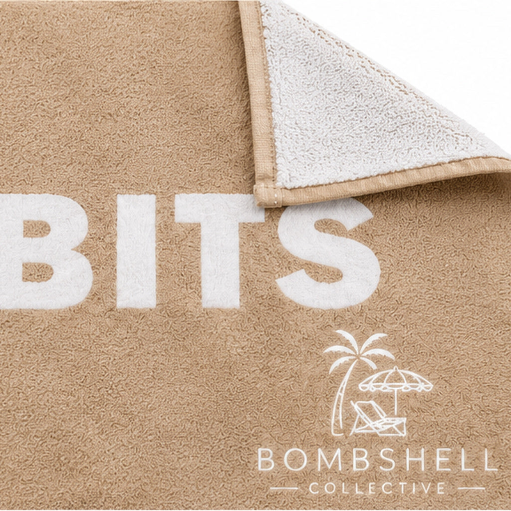 Close-up of the Face Bum Bits bath towel in Sand showing textured fabric, stitched edges, folded white reverse and Bombshell Collective logo.